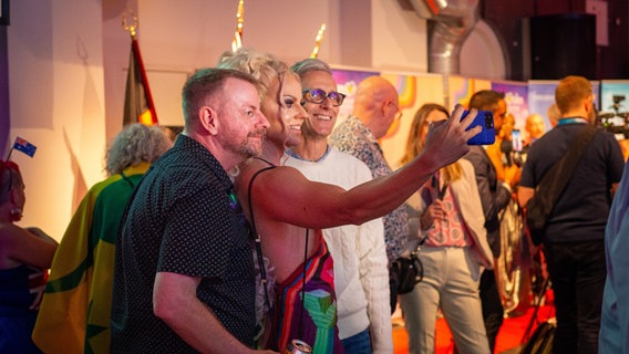 Host Courtney Act macht ein Selphy mit zwei Gästen auf der Australischen Eurovision Party. © NDR Foto: Margarita Ilieva