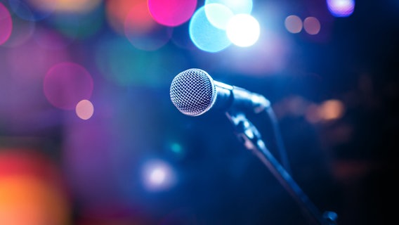 Ein Mikrofon auf einer Bühne zwischen bunten Lichtern. © fotolia.com Foto: Saon168, Andrey Armyagov