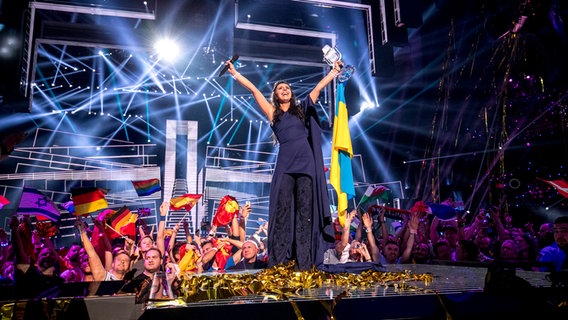 Jamala aus der Ukraine hält den ESC-Pokal und eine Flagge in die Höhe. © NDR/eurovision.tv Foto: Andres Putting (EBU)