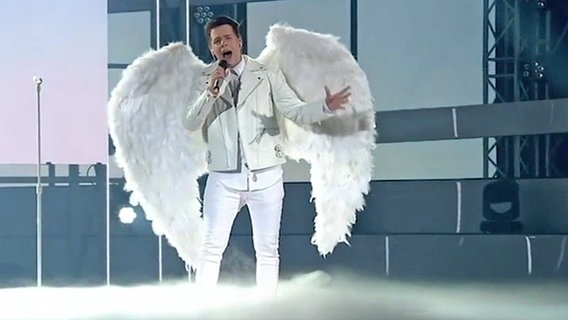 Der kroatische Sänger Roko steht mit Engelsflügeln auf einer Bühne.  