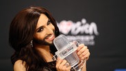 Die Sängerin Conchita Wurst hält ihren ESC-Pokal bei einer Pressekonferenz vors Gesicht © NDR Foto: Rolf Klatt