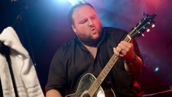 Der Musiker Alex Diehl mit seiner Gitarre auf einer Bühne. © dpa Foto: Britta Pedersen