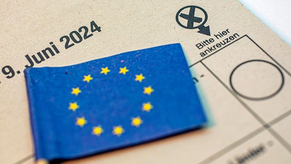 Auf einem Wahlzettel für die Europawahl liegt eine kleine EU-Flagge. © dpa picture alliance/Goldmann 
