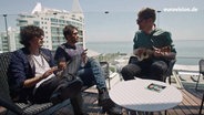 Ermal Meta, Fabrizio Moro und Stefan Spiegel sitzen auf einer Dachterasse in Lissabon. © NDR 