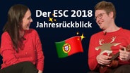 Alina Stiegler (li.) und Stefan Spiegel lachen sich an, gekleidet in rote Weihnachtspullis.  