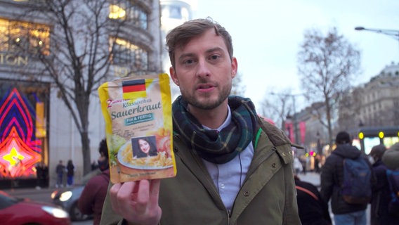 Consi mit einer Packung Sauerkraut in der Hand auf der Champs Élysées. © NDR Foto: Screenshot