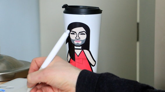 Eine Hand hält einen Stift, dahinter ein Kaffeebecher  Foto: Kathrin Otto