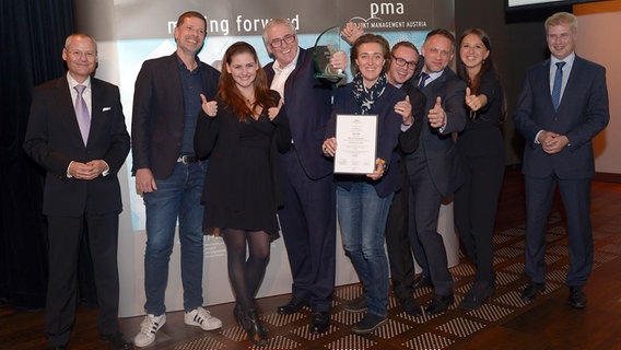 Das ORF Team präsentiert den gewonnenen pma award vor einer Fotowand stehend. © pma 