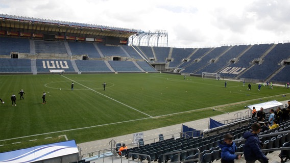 Ein weitestgehend leeres Fußballstadion, in dem sich Spieler vor dem Spiel aufwärmen.  