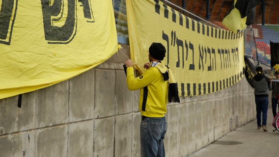 Ein Fan bringt die Flagge des Vereins Beitar Nordia im Stadion an  
