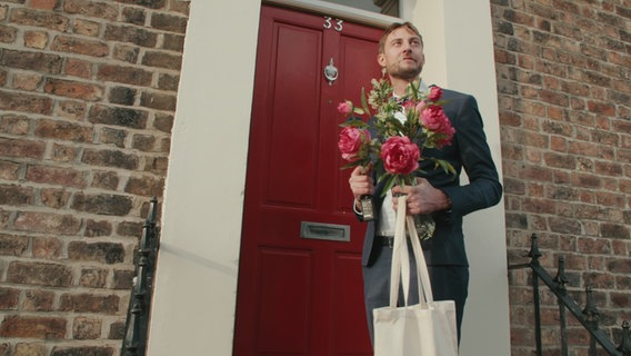Consi klingelt mit Blumen an einer Haustür. © NDR Foto: Screenshot