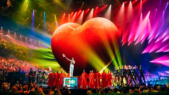 Moderator Mika steht vor einem großen roten Herz auf der Bühne in Turin. © eurovision.tv/EBU Foto: Sarah Louise Bennett
