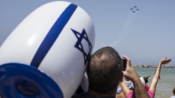 Ein Mann mit einem aufblasbaren Hammer mit Israel-Flagge schaut am Strand von Tel Aviv der Flugshow der Armee zu. Unabhängigkeitstag in Israel. © dpa Foto: Ilia Yefimovich