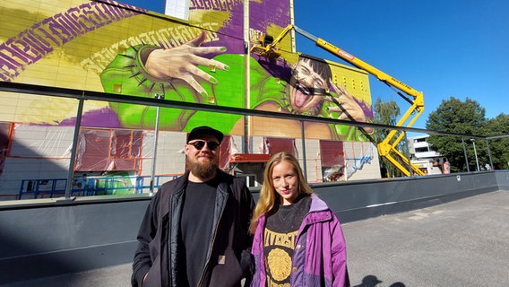 Die Künstler Juha Lahtisen und Viivi "Viv Magia" Vierisen vor ihrem Wandgemälde von Käärijä in Vantaa. © NDR Foto: Daniel Kähler