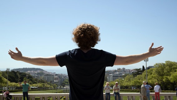 Michael Schulte bereitet beide Arme aus und schaut auf Lissabon. © NDR / Rolf Klatt Foto: Rolf Klatt