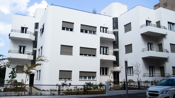 Ein schlichtes, weißes Gebäude im Bauhaus-Stil steht am Straßenrand.  