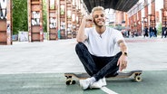 Malik Harris sitzt lachend auf einem Skateboard in Turin. © NDR Foto: Claudia Timmann