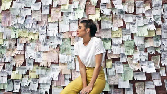 Die französische Sängerin Alma sitzt vor einer Wand mit vielen Papierzetteln. © Warner Music 