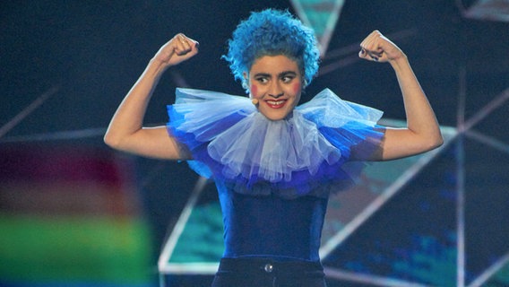 Die australische ESC-Teilnehmerin Montaigne steht mit blauer Halskrause, blauen Haaren und Clownsschminke auf der Bühne. © SBS 