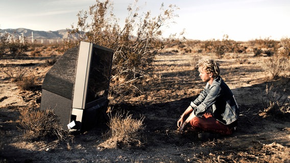 Finn Martin sitzt in der Wüste vor einem Fernseher. © EMI Music Germany Foto: Lennart Brede