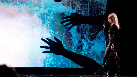 Gréta betritt die Bühne, hinter ihr sind schwarze Hände auf einen bunten Hintergrund projiziert. © eurovision.tv Foto: Andres Putting (EBU)