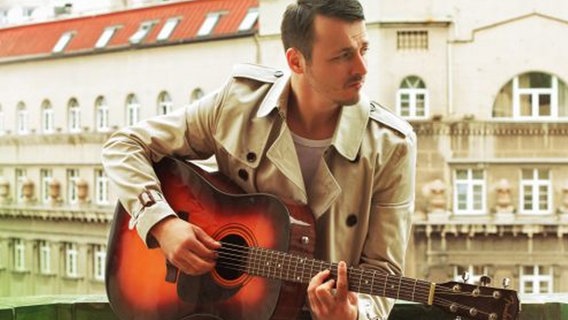 Daniel Kajmakoski sitzt auf einer Balkonbrüstung und spielt auf einer Akustikgitarre.  Foto: Andreja Damjanovic