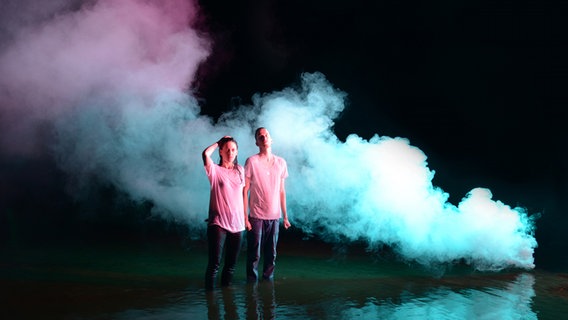 Kat Frankie und Chris Klopfer von Keøma stehen in rosa T-Shirts vor bunten Dampfwolken © Embassy of Music Foto: Andreas Wisskirchen