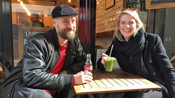 Die deutsche ESC-Kandidatin Levina und Bürger Lars Dietrich sitzen vor einem Cafè in London. © NDR Foto: Jürgen Werwinski