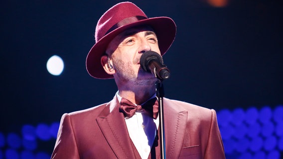 Serhat steht im burgunderfarbenen Anzug vor dem Mikrophon. © eurovision.tv Foto: Thomas Hanses (EBU)