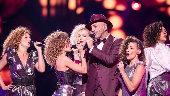 Der ESC-Künstler Serhat im rostrocken Frack mit Zylinder steht umzingelt von singenden Frauen auf der Bühne des ersten Halbfinale © NDR Foto: Rolf Klatt