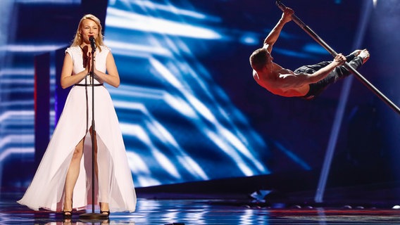 ManuElla steht am Mikrophon und ein Tänzer wirbelt um eine Stange. © eurovision.tv Foto: Andres Putting (EBU)