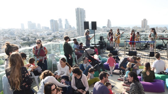 Vielen Menschen hören auf einer Dachterrasse in Tel Aviv einer Band zu  