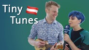 Stefan Spiegel hält eine Ukulele in der Hand, die österreichische ESC-Teilnehmerin Paenda steht mit einem Mikro neben ihm. © NDR 