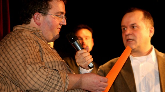 OGAE-Fan Frank Bischof (links) verkündet als lebende Anzeigentafel und mit Hilfe von Reinhard Ehret das Ergebnis des Karaoke-Wettbwerbs. © NDR Foto: Marco Lambrecht