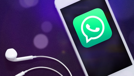 Das Logo von WhatsApp ist auf einem Handy abgebildet, daneben liegen Kopfhörer © Kostya Klimenko 