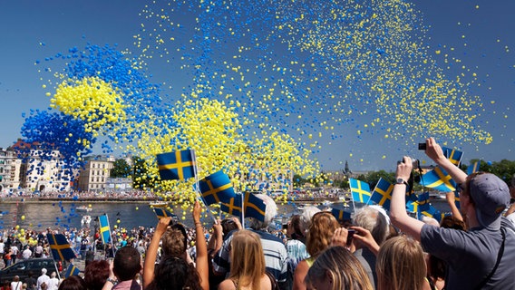 Menschen schwenken Schweden-Flaggen und blaue und gelbe Luftballons steigen in den Himmel © Ola Ericson_imagebank.sweden.se Foto: Ola Ericson